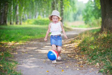 curly blonde girl playing with a rubber ball in a summer park