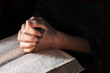 Hands clasped in prayer near an open book