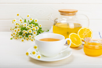 Chamomile herbal tea with flower buds, honey and lemon on a white wooden table and a bouquet of chamomile. Useful herbal, soothing drinks and natural healer concept. Immunity tea.Close up. Copy space. - obrazy, fototapety, plakaty