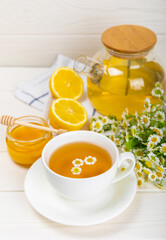 Chamomile herbal tea with flower buds, honey and lemon on a white wooden table and a bouquet of chamomile. Useful herbal, soothing drinks and natural healer concept. Immunity tea.Close up. Copy space.
