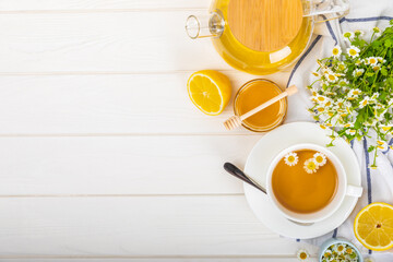 Chamomile herbal tea with flower buds, honey and lemon on a white wooden table and a bouquet of...