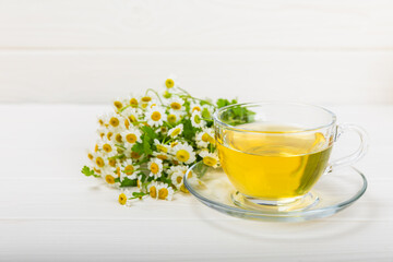 Chamomile herbal tea with flower buds, honey and lemon on a white wooden table and a bouquet of chamomile. Useful herbal, soothing drinks and natural healer concept. Immunity tea.Close up. Copy space.