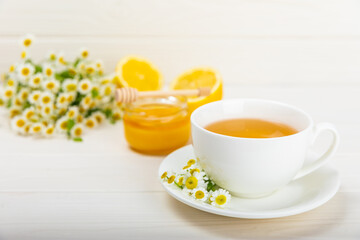 Fototapeta na wymiar Chamomile herbal tea with flower buds, honey and lemon on a white wooden table and a bouquet of chamomile. Useful herbal, soothing drinks and natural healer concept. Immunity tea.Close up. Copy space.