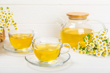 Chamomile herbal tea with flower buds, honey and lemon on a white wooden table and a bouquet of chamomile. Useful herbal, soothing drinks and natural healer concept. Immunity tea.Close up. Copy space.