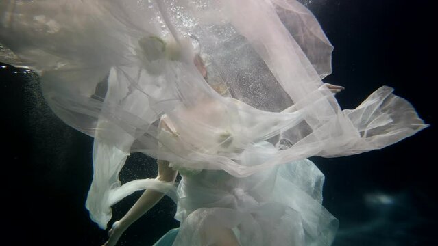 fabulous princess swimming underwater, magical female figure in dark depth, slow motion portrait