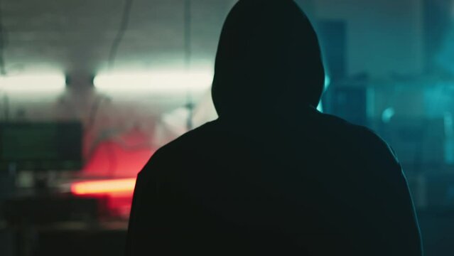 Mysterious cyber security hacker in hoodie in headquarter with computers
