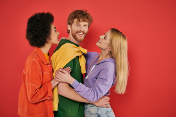 polygamy concept, interracial lovers showing hugging each other on coral background, cultural diversity, polyamorous, happy multiethnic people, looking at camera, open relationship