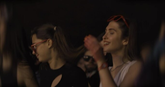 girls dancing in crowd in front of stage with flashing lights..
