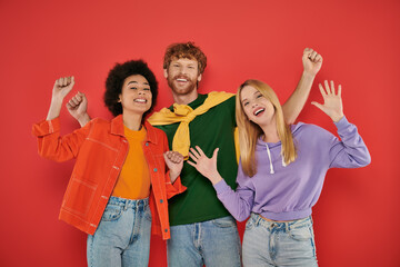 polyamorous concept, polygamy lovers, young man and multicultural women celebrating on coral background, studio shot, denim fashion, love triangle, bonding and acceptance
