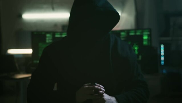Mysterious cyber security hacker in hoodie in headquarter with computers