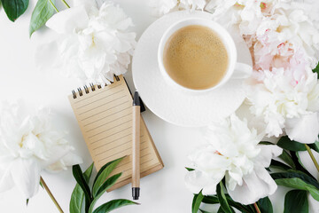 Top view of coffee cup, notebook, pen and pionies