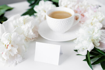Coffee cup, card and white pionies on table