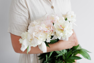 Woman holding white fresh peony bouquet in hands