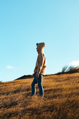 A young man side portrait with a cream hoodie in dry grass and blue sky background from golden hour sunset, puerto rico