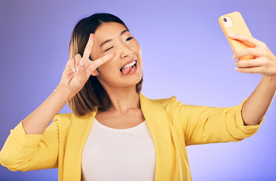 Asian woman, peace sign and funny face for selfie, photo or memory against a purple studio background. Happy female person or model pose with peaceful emoji, goofy or silly for picture or online vlog - Powered by Adobe