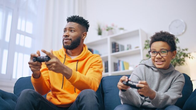 Two African American brothers playing video game together at home, cheerful siblings