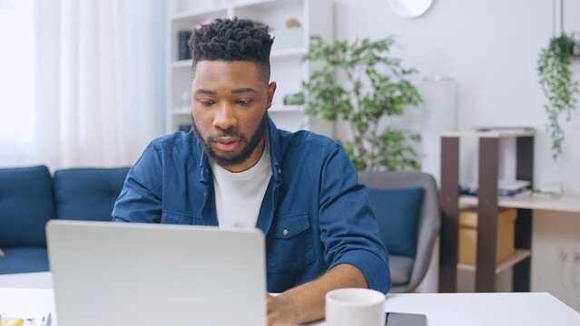 Young African American man working from home using laptop, freelancer's lifestyle, writer