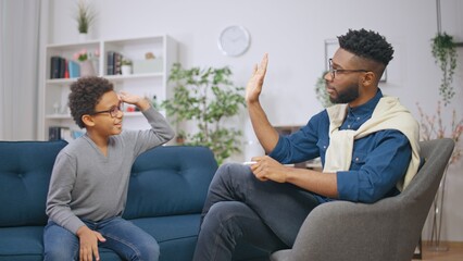 Positive male psychologist finishing counselling session with a child, giving boy a high five,...