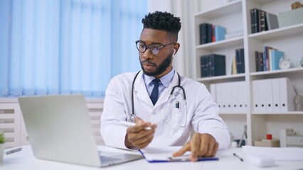African American practitioner counselling patient via video call, writing down notes