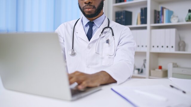 Close-up of young African doctor working on laptop, online consultation, job