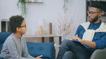 Psychologist consulting little African American boy, child therapy session, troubled youth counselling