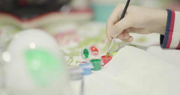 Boy making custom Christmas decorations. Painting green tree on white crystal or plastic ball.