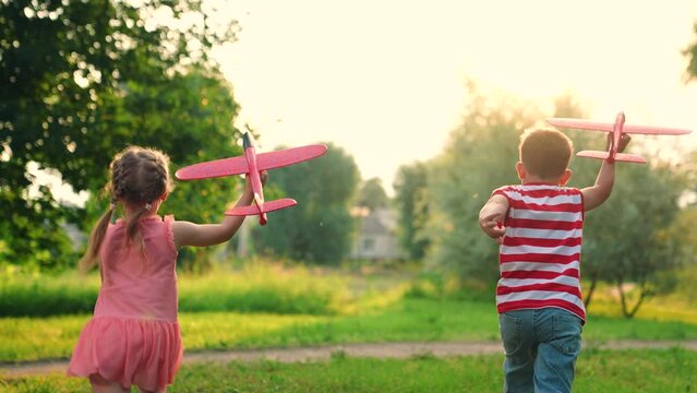 Child, boy, girl play in park, friends run together, dream of flying. Children play run fly with toy plane in sky. Airplane imagination of children, concept of active play in nature. Holiday family.