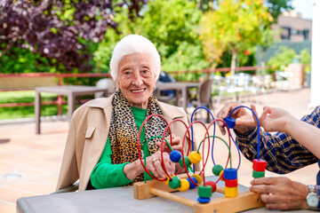 An elated elderly woman sits in a gorgeous geriatric garden, playing a children's hand motor skills...