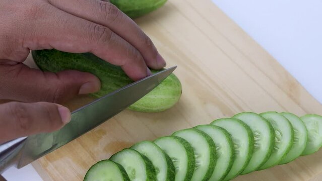 hand slicing cucumber on wooden cutting board