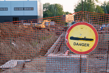 Shabby danger sign on the background of construction site and excavator