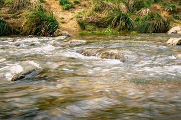 Rapid and powerful water flow between large rocks, close-up. Boulders in cold mountain river. Natural backgrounds