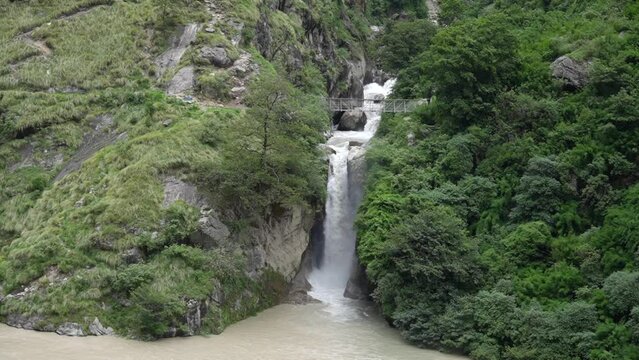 Waterfall cascades over a white-water river that originates from glaciers amidst the forest.