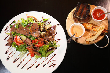 Salad with beef tongue with vegetables and herbs, dressed with sauce on a white plate.
