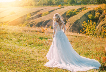 Fototapeta premium happy beautiful joyful bride walking in hills, long train white dress back rear view mystery silhouette,no face. Girl blonde hair. autumn nature green grass trees divine magic sun light wedding day