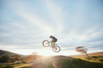 Fototapeta na wymiar Fitness, cycling and person with bicycle jump for extreme sports and energy on blur mockup space . Action, bike and cyclist athlete in the countryside with speed, trick and skill, adventure or power