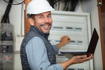 electrician with computer checking fuse box