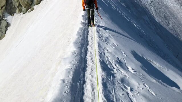 Сlimber walking narrow path on mountain ridge under Aiguille du Midi 3842m with French Alps mountains peaks panorama. Beauty of Nature and extreme people activity concept