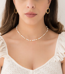Young woman wearing golden earrings and a mother of pearl necklace.