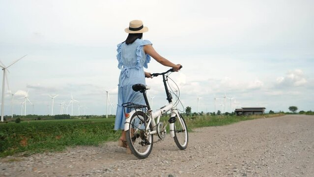 Woman in dress enjoying a leisurely bike ride Among the wind turbines in the background. Confident middle aged woman enjoying strolling outdoors.