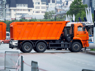 A red dump truck stands across the road, blocking it. Urban background with big truck.