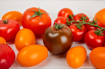 Tomatoes on a white wooden background. Cherry tomatoes, yellow, pink, brown and black tomatoes in a bowl. Organic vegetables, harvesting.Vegan. Fresh ripe tomatoes. copy space.