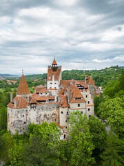 Obraz premium Medieval Bran Castle, aerial drone perspective. Known as Dracula's Castle, it is visited annually by many foreign tourists. One of the best-known tourist attractions of Romania. Vertical photography.