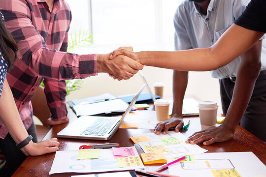 Close up of two tech engineers shaking hands at design launch meeting mobile app