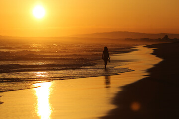 A serenidade do entardecer na praia do Algarve, em Portugal. Uma mulher caminha descalça em...