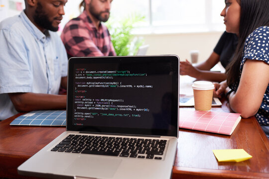Close up of laptop screen with code, developers meeting boardroom table talking