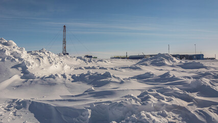 The Northern gas field. There is a lot of snow in the foreground. In the background is a mobile installation for well repair. A frosty winter day. Sunny blue sky