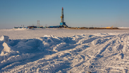 A gas field in the Arctic. Polar winter day. In the foreground is a snowy tundra. In the background is a drilling rig and industrial infrastructure