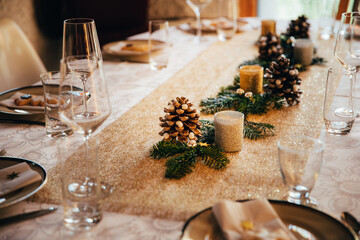Dinner table festively decorated with candles and pine cones to celebrate Christmas Eve.