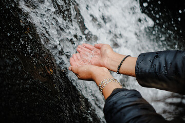 woman's hands touching the water of a cold waterfall in the andean mountains