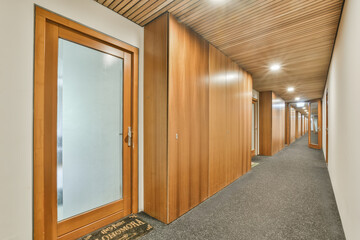 an office hallway with wood paneled walls and glass door leading to the first floor, which is lined with grey carpet
